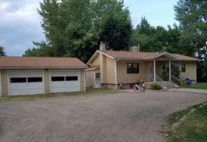 A house with two garage doors and trees in the background.