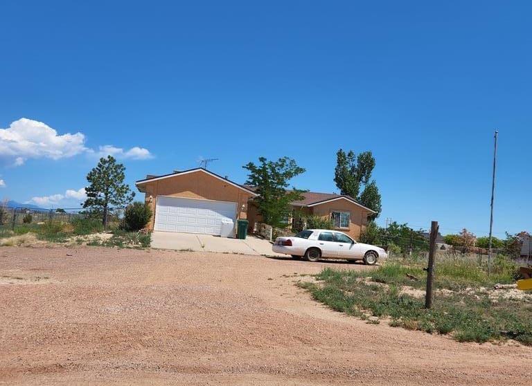 A car parked in front of a house on the side of a dirt road.